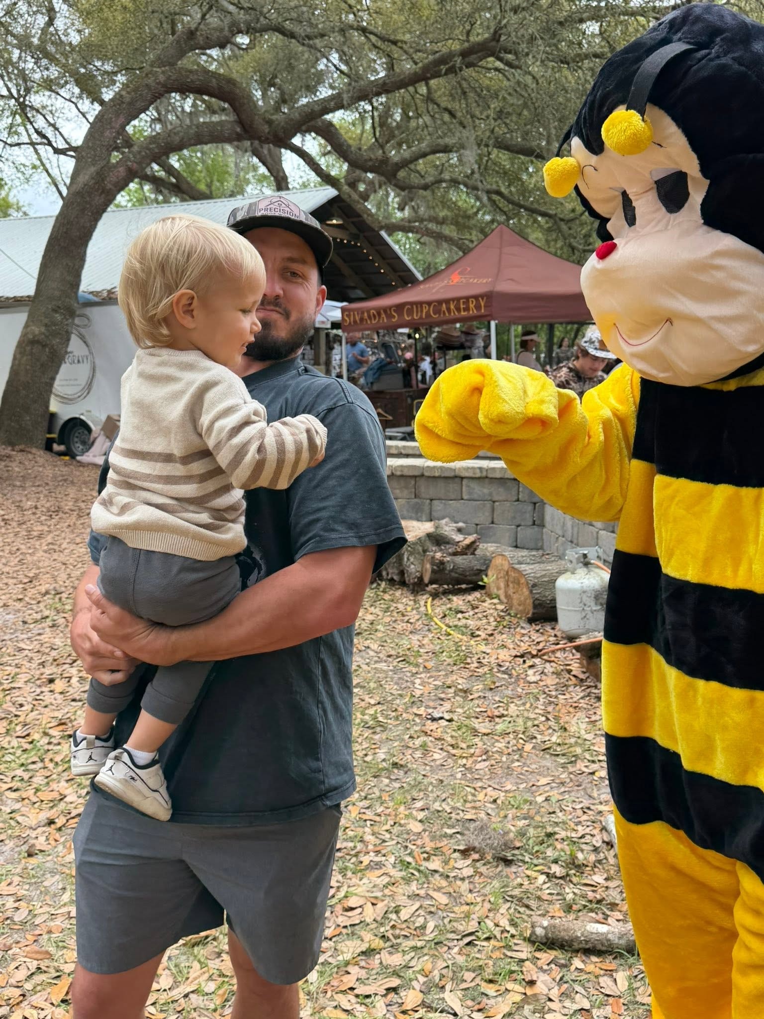 Dad holding toddler while an AC Bee mascot reaches out to greet them