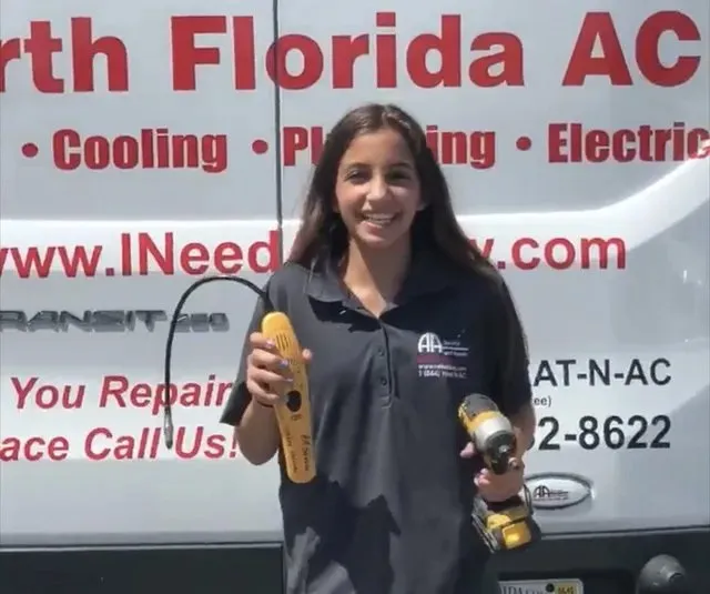 Woman holding power tools smiling in front of a business sign.