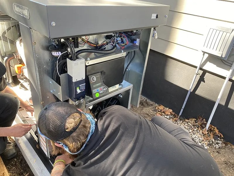 Technician repairing an open HVAC unit outside a house.